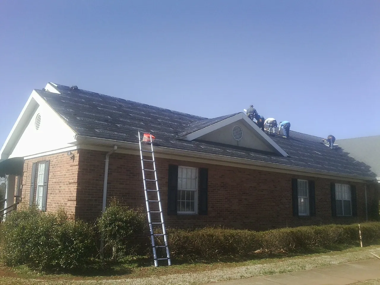 Crew tearing shingles off a brick ranch roof with a ladder set — Metal Roof Repair work by our crew in Whigham