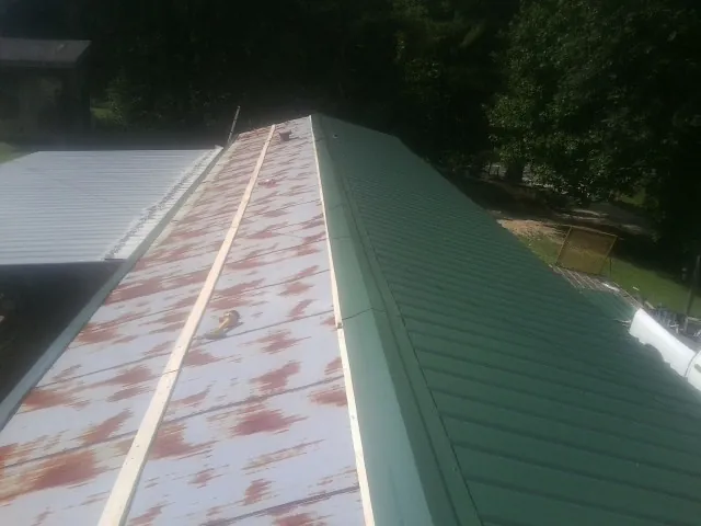 Old rusted panels beside newly installed green metal roofing — Wind Damage Roof Repair by Roofing Brothers in Whigham