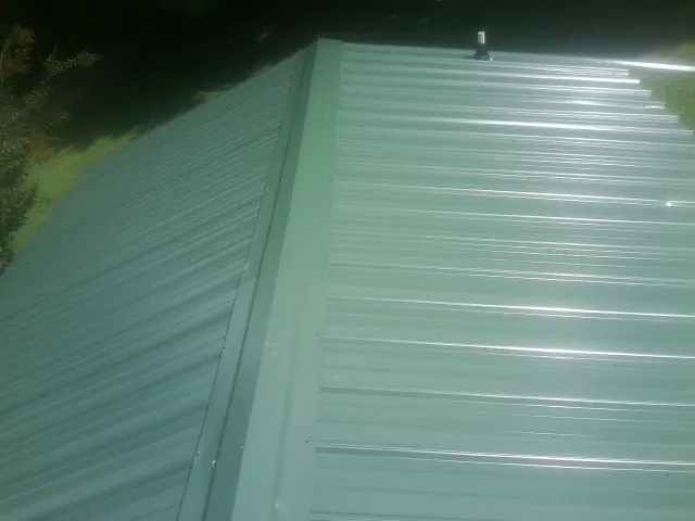 New green metal panels meeting at the ridge of a roof — Flat Roof Repair work by our crew in Whigham