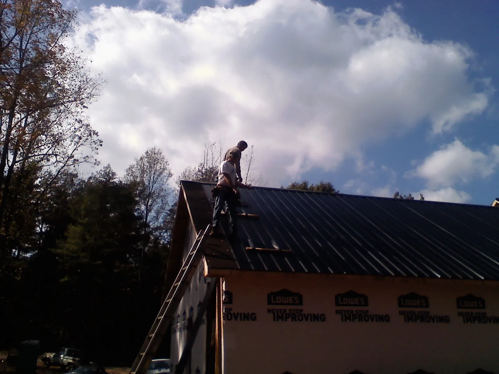 Roofer fastening dark metal panels high against a cloudy sky, from a Roof Inspection job in Whigham