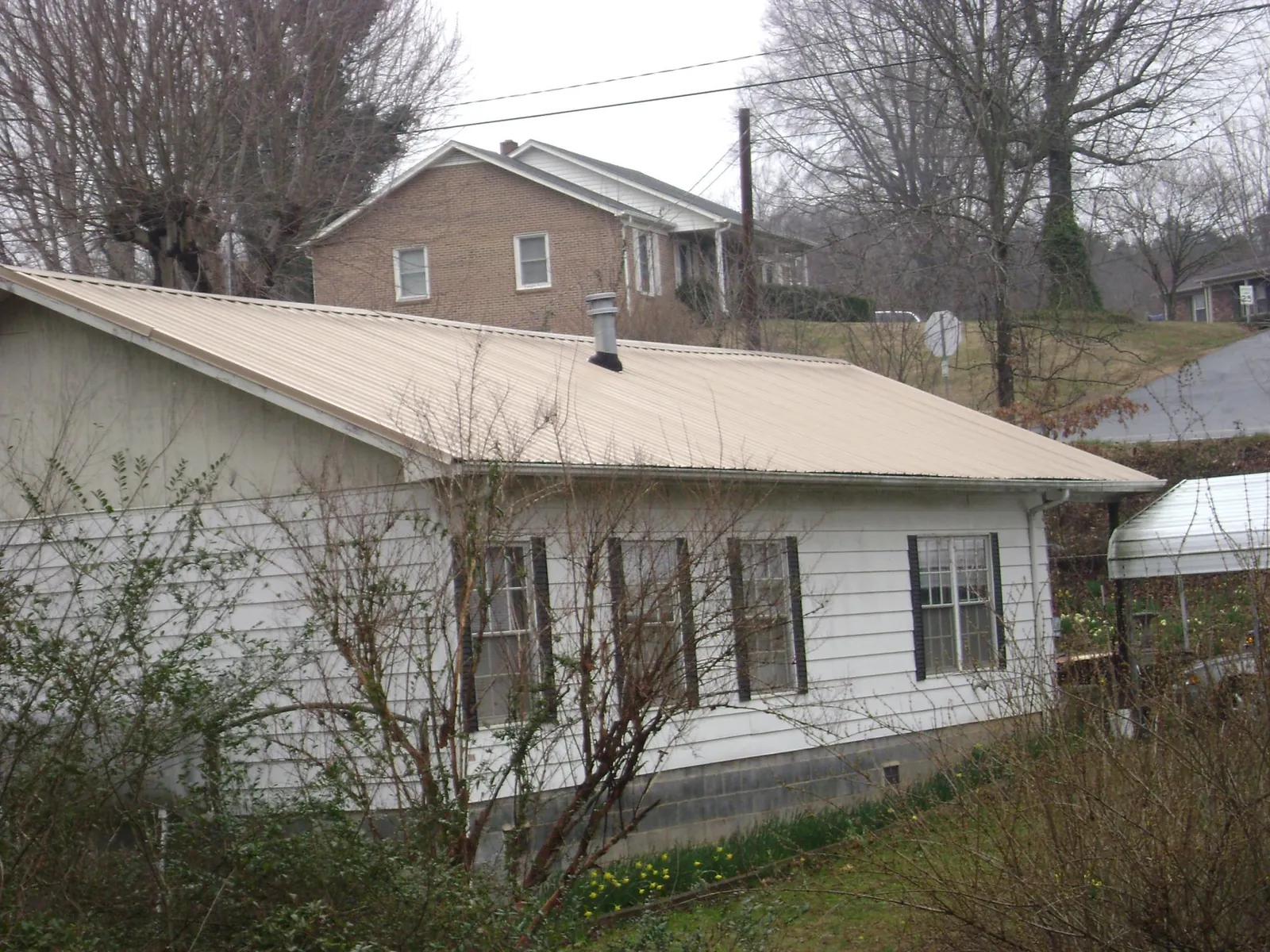 Tan metal roof on a white sided house set into a hillside — Commercial Roofing by Roofing Brothers in Whigham