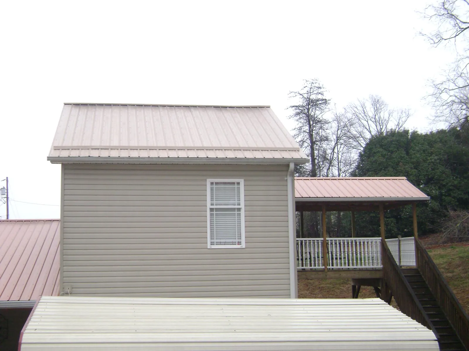 Tan metal roofs on a two story addition and attached porch, from a Roof Replacement job in Whigham
